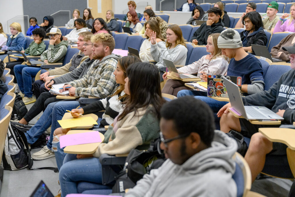 A classroom full of students, taking notes and listening to their professor